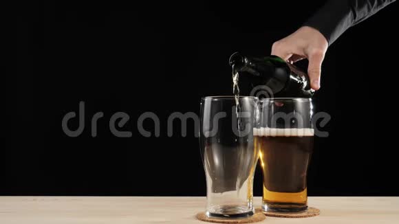 新鲜啤酒手把美味的手工啤酒倒在第二杯啤酒杯上从棕色的瓶子里倒入木桌上放在黑色的桌子上视频的预览图