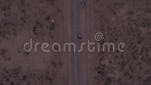 鸟瞰飞行在孤利废弃的沙漠道路上红色汽车在远处行驶视频的预览图