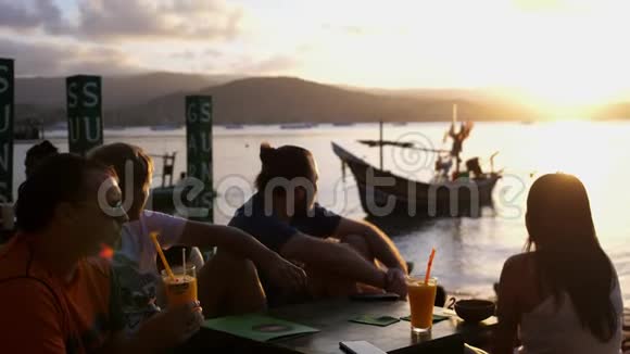 朋友们坐在山上的咖啡馆里俯瞰大海令人惊叹的日落喝鸡尾酒慢动作视频的预览图