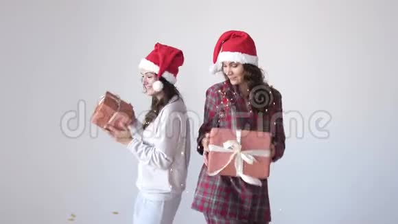 穿着圣诞帽和睡衣跳舞和摇动礼盒的快乐女人假日概念惊喜视频的预览图