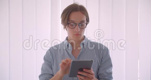 一位年轻英俊的白种人商人戴着眼镜用平板电脑站在办公室的室内特写肖像视频的预览图