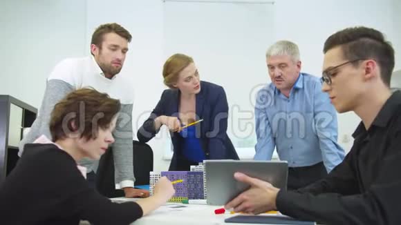 年轻人坐在桌旁桌上放着平板电脑他的同事看着并讨论视频的预览图