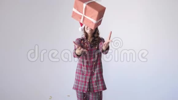 穿着圣诞帽和睡衣的快乐女孩在白色背景下扔礼物盒等待假期慢动作视频的预览图