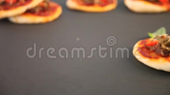 女人的手把自制的迷你披萨放在黑板上迷你比萨饼上面有火腿绿色橄榄樱桃番茄和新鲜罗勒视频的预览图