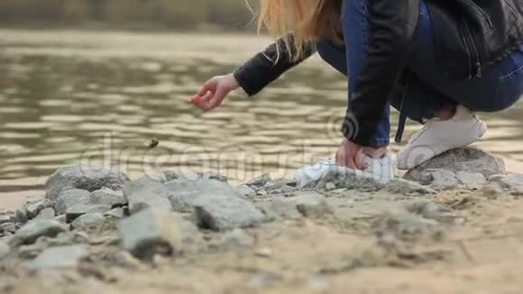 女人的手把一块石头扔进河岸上的水中视频的预览图
