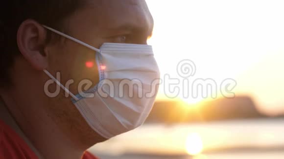 日落时分一个蒙面的年轻悲伤男子坐在海滩上冠状病毒流行视频的预览图