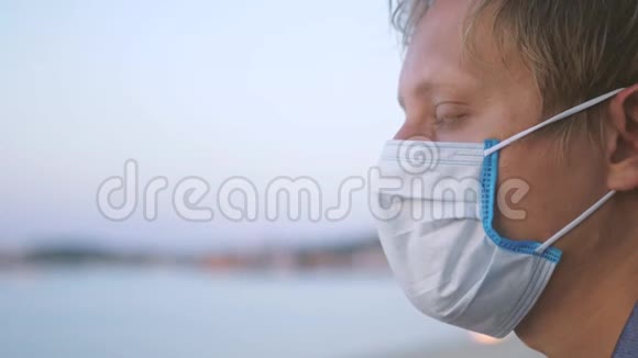 戴着医用面具的年轻人在海滩上沉思冠状病毒流行视频的预览图