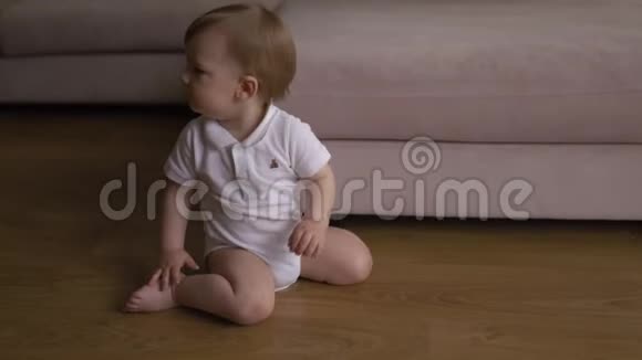 小男孩坐在家里的地板上感到困倦和好奇孩子穿白色t恤身体马球视频的预览图
