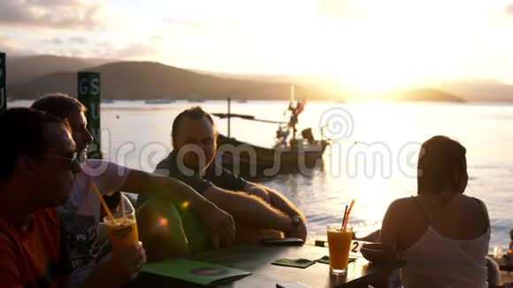 朋友们坐在山上的咖啡馆里俯瞰大海令人惊叹的日落喝鸡尾酒慢动作视频的预览图