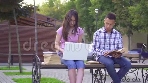 年轻的亚洲学生男人拿着一本书女人拿着一台笔记本电脑坐在长凳上慢悠悠视频的预览图