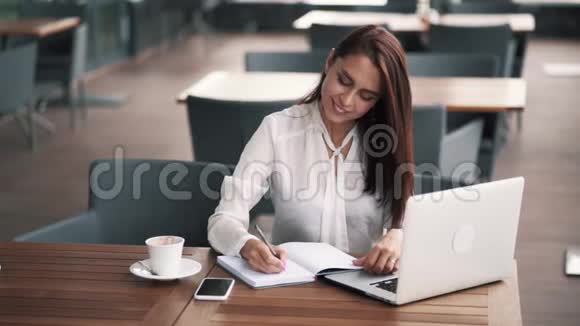漂亮的白衬衫女孩在咖啡馆工作在笔记本上写字慢动作视频的预览图