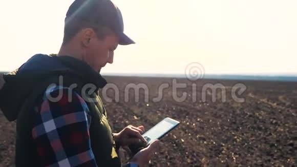 男子农民红脖子与数字平板行走在土地上缝纫在土壤黑田生态农业视频的预览图