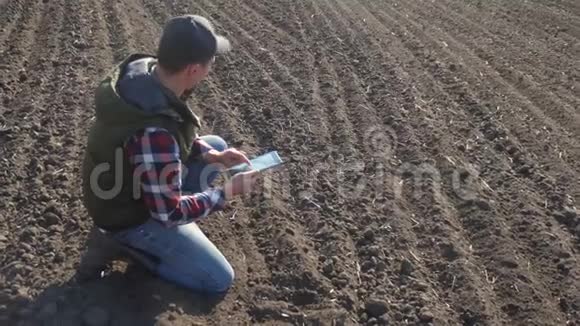 男子农民生活方式红脖子与数字平板行走在土地上缝纫在土壤黑田生态农业视频的预览图
