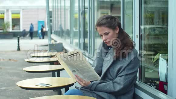 一个穿着灰色毯子在咖啡馆里看报纸的女孩的侧视视频的预览图
