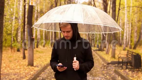 一位带着手机的年轻人在雨天沿着秋天公园散步的肖像视频的预览图