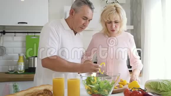 年长的男人帮成熟的妻子把切好的胡椒放进沙拉碗里视频的预览图