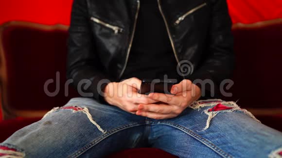 年轻人拿着智能手机躺在红色的小沙发上男性身体部位的特写坐在扶手椅上手机在视频的预览图