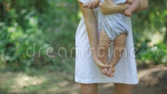 年轻漂亮的母亲抱着她的新生女儿在一个公园的绿色树叶背景慢动作年轻快乐视频的预览图