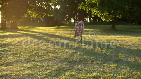 穿着五颜六色的花裙穿过公园的草地的少女视频的预览图