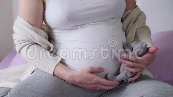 穿着白色t恤坐在床上抱着的怀孕女孩视频的预览图