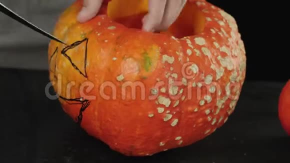 准备在万圣节制作灯笼手在木桌上的橙色南瓜上为眼睛切割一个洞视频的预览图