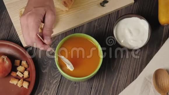 奶油南瓜汤烹饪把酸奶油放在奶油南瓜汤里放在绿色的碗里放在装饰好的木桌上上景4K视频的预览图