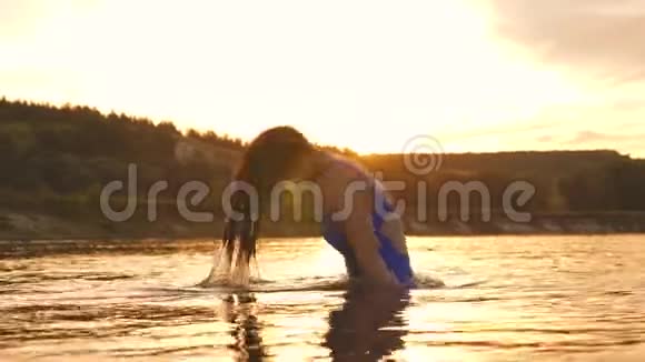 一个年轻的女孩留着长发洗澡日落时泼水快乐和欢笑的女人在河里凉快夏季视频的预览图