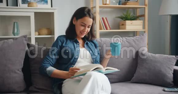 慢动作吸引人的女孩在家拿着一杯咖啡看书视频的预览图