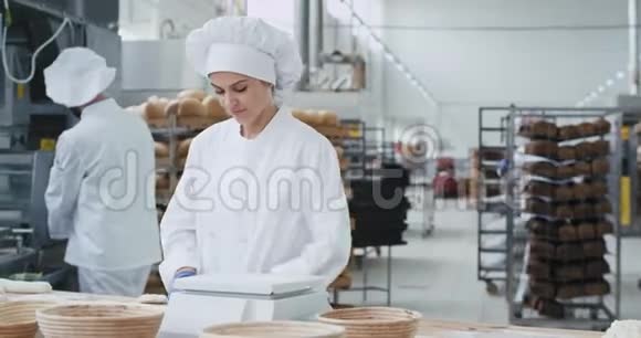 集中精力的漂亮女人面包师在她的电脑上工作形成面团用来烘焙面包而其他工人视频的预览图