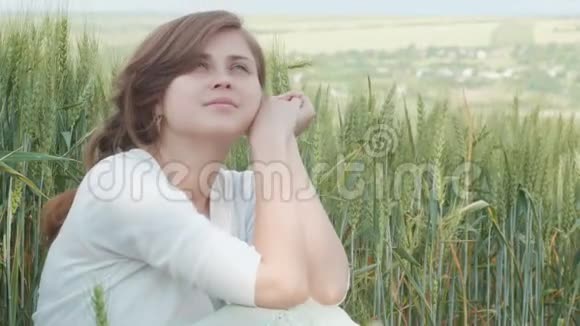 美丽的年轻女孩坐在田里高高的绿色小麦穗之间年轻快乐的女人享受夏天和谐视频的预览图