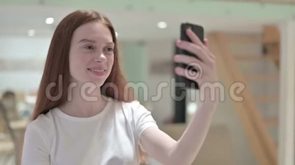 红头发青年妇女在智能手机上视频聊天的画像视频的预览图