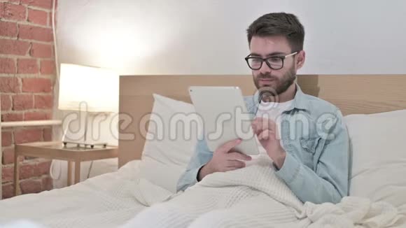 年轻男性设计师在床上使用平板电脑视频的预览图