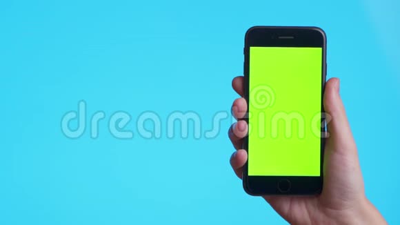 女人手拿着一部蓝色背景上带有greeen屏幕的智能手机只收手的镜头视频的预览图