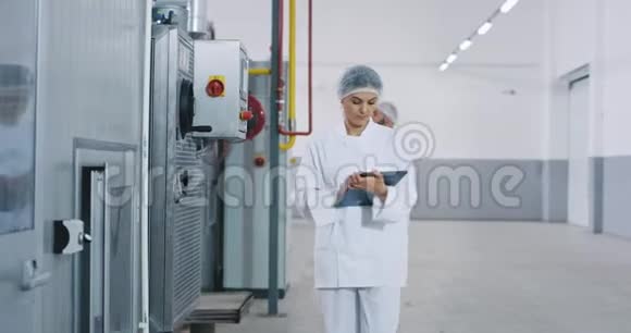 在一家大的面包店里一位商业工程师女士正在检查一台工业机器她在里面做了一些笔记视频的预览图