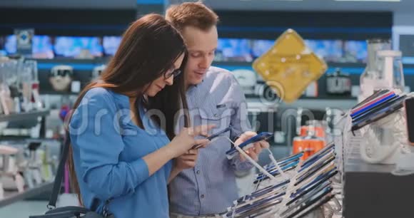 一个年轻的男人和女人手里拿着两部智能手机站在一个电子产品智能手机陈列柜旁视频的预览图