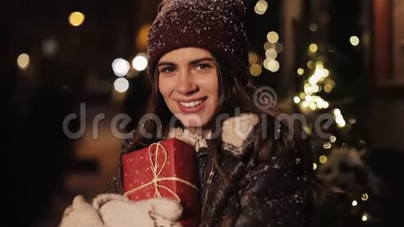特写年轻漂亮女孩的肖像看着快乐拿着礼品盒和微笑站在落雪的户外视频的预览图