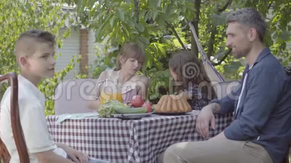 爸爸妈妈和他们的两个孩子坐在一张桌子旁在花园里吃午饭享受着阳光明媚的一天家庭调查视频的预览图