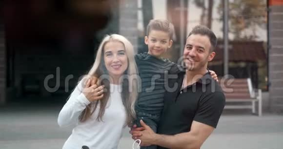 户外微笑幸福家庭的肖像带着孩子的父母正在看镜头视频的预览图