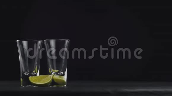在旋转的黑板上用两个玻璃杯在黑色背景上倒入金色龙舌兰倒酒喝伏特加龙舌兰关闭视频的预览图
