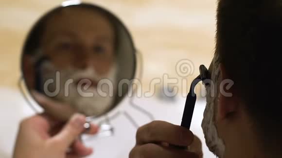 年轻英俊的男人在浴镜里刮胡子每天的护肤仪式视频的预览图