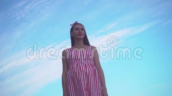 穿着条纹红白连衣裙的年轻女孩一个女孩站在蓝天上举起双手象征着自由视频的预览图