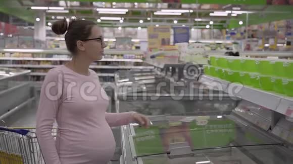 一个年轻的孕妇带着眼镜在超市选择塑料盘子储存女人选菜视频的预览图
