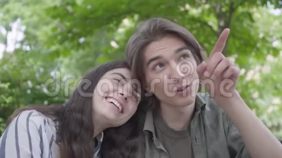 一对年轻微笑的夫妇穿着休闲服装在公园里聚在一起约会他指指点点视频的预览图
