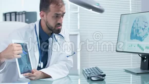 医生在温和的办公室与玻璃桌交谈并指向一个数字平板电脑屏幕上的X射线视频的预览图
