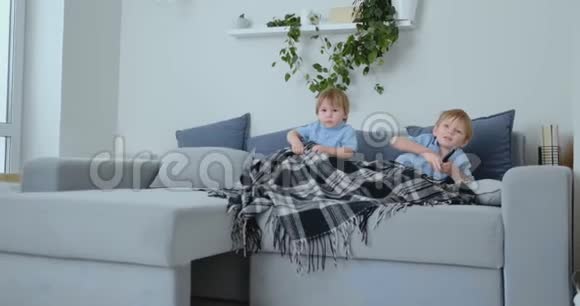 两个男孩4岁和2岁坐在沙发上看电视令人兴奋的电视节目观看漫画视频的预览图