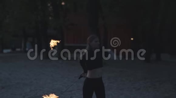 令人敬畏的自信女孩与苗条的身体表演一个表演与火焰站在树前有技巧的消防艺术家视频的预览图