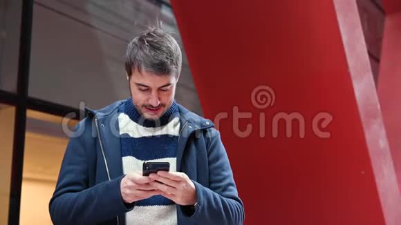 英俊的年轻人站在办公楼外一边用手机上网一边休息视频的预览图