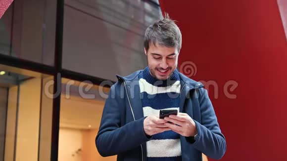 英俊的年轻人站在办公楼外一边用手机上网一边休息视频的预览图