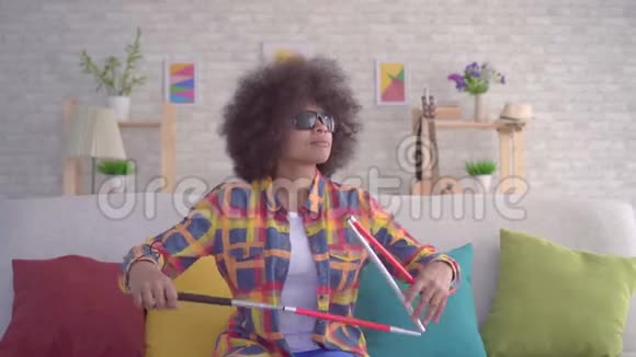 非洲妇女发型为非洲戴眼镜视障手拿拐杖坐在沙发上视频的预览图