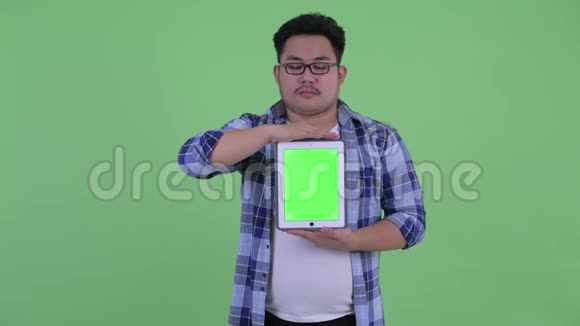 年轻体重超重的亚洲时髦男士展示数码平板电脑视频的预览图